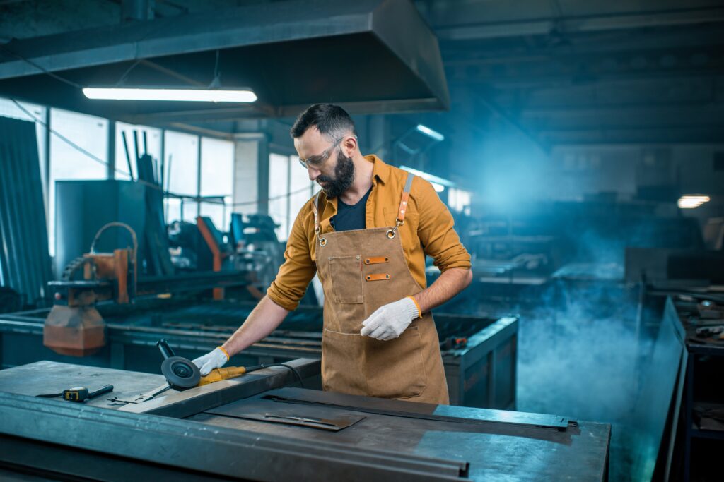Metal industry worker in apron using tools on sheet metal in a fabrication workshop, demonstrating precision and craftsmanship for custom ductwork and industrial solutions.
